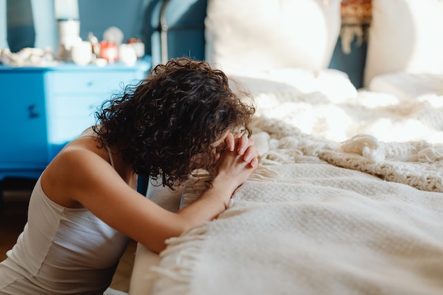 A woman kneeling praying in front of her bed connecting with God