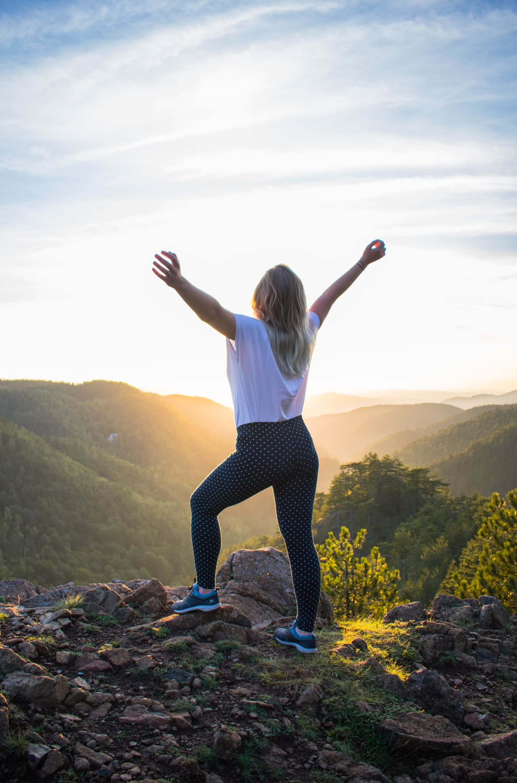 Woman in the white shirt & black pants standing on rocky mountain during the day-inspire appreciation for the outdoors.