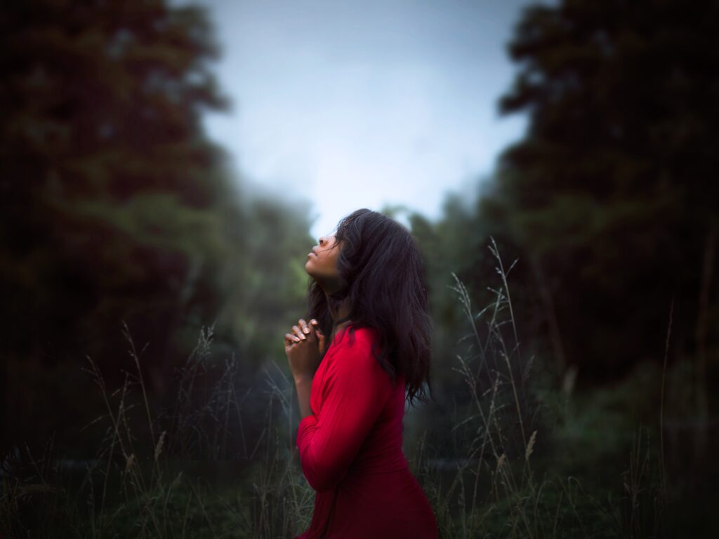 A woman with a red dress stand in the field praying