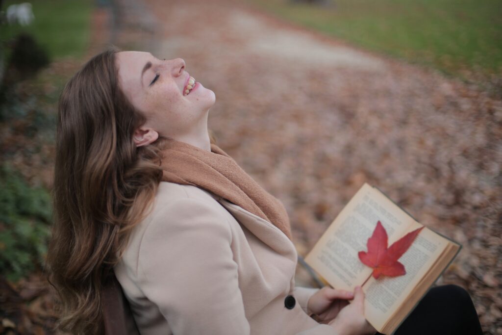 A happy woman holding a book laughing while sitting conveys a positive message of happiness.