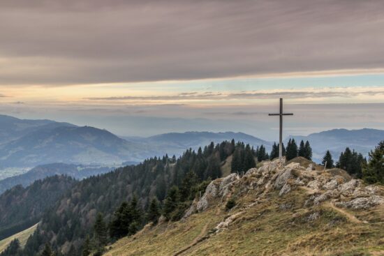 A cross atop a mountain surrounded by nature, representing the faith and hope of God's children.