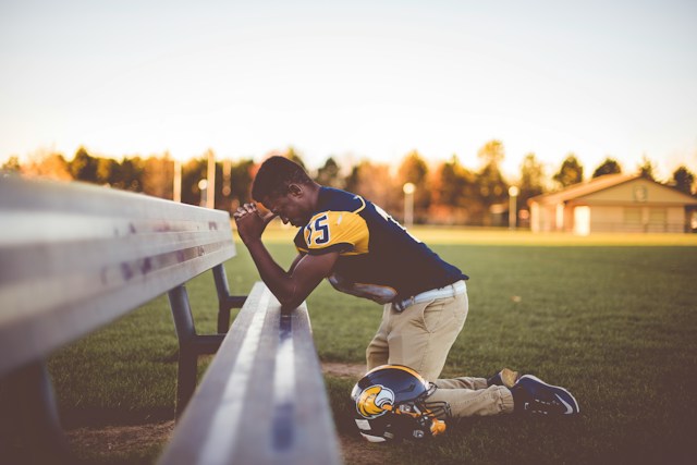 Baseball player kneeling on the ground, praying the Lord's Prayer.