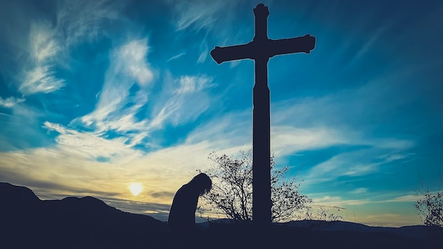 A person kneeling down in front of a cross, reflecting on forgiveness through The Lord's Prayer.