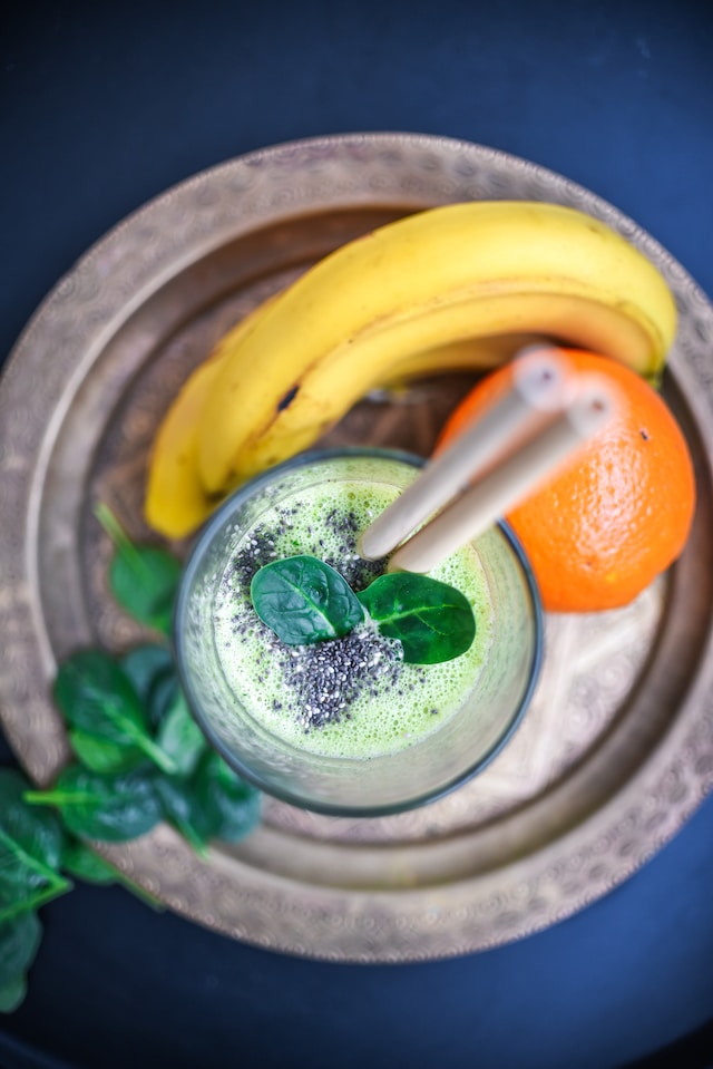 a glass of green smoothie with bananas & oranges