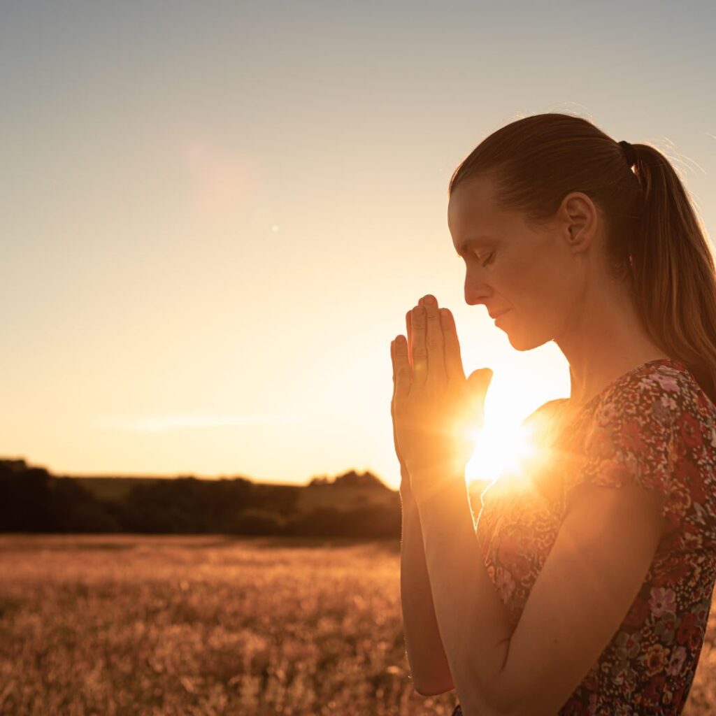 A Godly woman praying in n a field at sunset