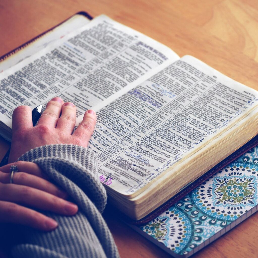 An open Bible with notes and highlights, a hand resting on it, and a nearby patterned notebook. Psalm 27