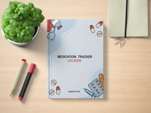 Medication Tracker Log Book by Angeline P. Utile on a wooden desk with pens, notebook, paperclips, and a potted plant — cover features medical illustrations like pills, syringe, and stethoscope